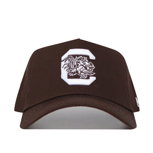 The South Carolina Americano Hat is a brown snapback with a large white "C" and detailed gamecock mascot embroidered on the front. Made from premium cotton, this structured cap offers lasting comfort and classic style.