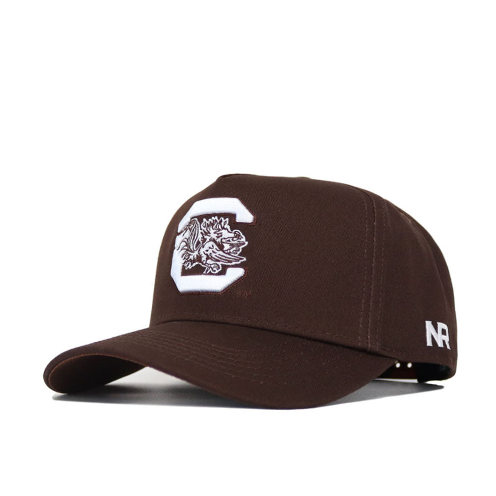 The South Carolina Americano Hat is a dark brown snapback with a large white C and gamecock logo on the front, NR letters in white on the side, and high-quality cotton construction for a structured fit.