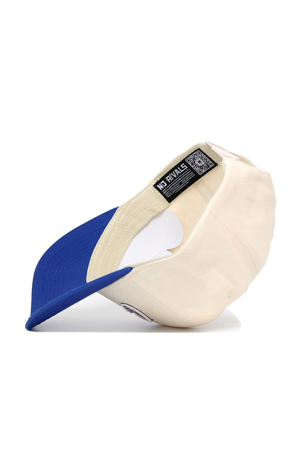 The Creighton Triangle Game Cap Hat by No Rivals is shown upside down, revealing its cream color, blue brim, and an inside label with the NO RIVALS brand name and a QR code.