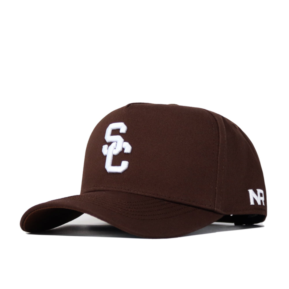 The USC Trojans Americano Hat features a brown snapback design with white embroidered "SC" on the front and "NR" on the side, crafted from premium cotton, and showcased stylishly against a white background.