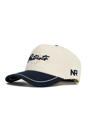 The No Rivals DBU Patriots ALOYO Hat is a beige and navy snapback with "Patriots" embroidered on the front, "NR" on the side, a white trim, structured fit, curved brim, and high quality cotton construction.