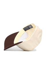 The Wyoming Triangle Game Cap Hat is a beige and brown snapback shown upside down, revealing its cream interior, sweatband, and black "NO RIVALS" tag with QR code. This structured cap is made from high-quality cotton for lasting comfort.