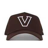 The Vanderbilt Americano Hat is a structured brown snapback cap made from premium cotton, featuring a large white embroidered "V" on the front and a curved brim. It is shown against a plain white background.