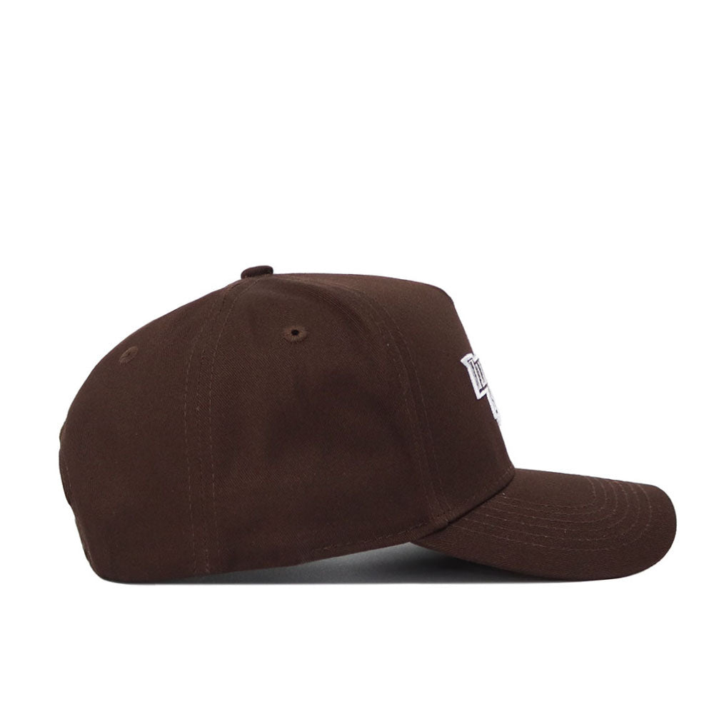 The Illinois State University Americano Hat is a brown structured baseball cap, shown from the side with a curved brim, dome with sewn eyelets, and part of a white embroidered logo on the front.