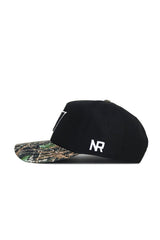 The No Rivals Vanderbilt Camo Hat - Trailblazer Edition features a black cotton design with a camouflage brim and white NR initials on the side. This snapback is displayed in side profile against a white background.