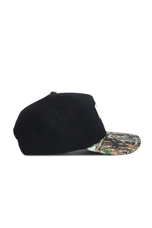 The No Rivals K-State Camo Hat - Trailblazer Edition is a high-quality black snapback with a camouflage brim, made from cotton and displayed from the side on a plain white background.