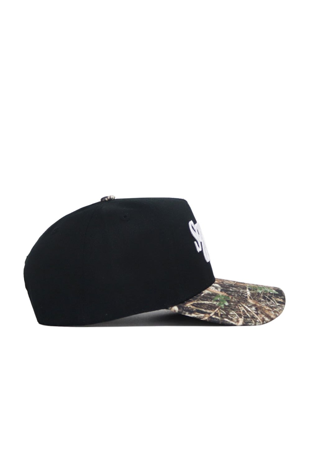 The Scheels Camo Trailblazer Hat is a black snapback with a camo-patterned brim, shown side-on against a white background. Made of high-quality cotton, it features partially visible white embroidered lettering on the front panel.