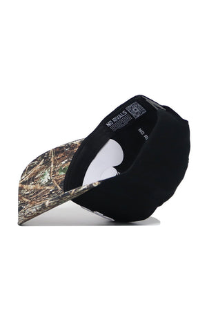 The Scheels Camo Trailblazer Hat is shown upside down, revealing "NO RIVALS" text and a QR code on the inner band. Its structured brim features a high-quality forest camouflage pattern in black and camo cotton.