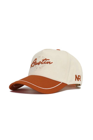 The Austin ALOYO Hat by No Rivals is a white and brown snapback with "Austin" embroidered in orange on the front and "NR" stitched on the side. Made from high-quality cotton, it features a structured fit and a brown brim with a white accent line.