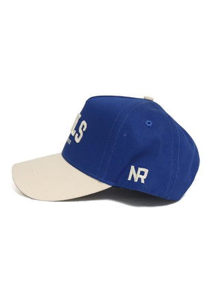 The OWLS Established Hat by No Rivals features a blue crown, beige brim, and white embroidered NR on the side with partial lettering on the front. It has a snap back closure for comfort and is shown on a white background—perfect for your gameday look.