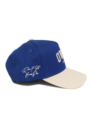 The No Rivals OWLS Established Hat features a blue crown, beige brim, white embroidered front text and side script. Its snapback design ensures a custom fit, while stitched eyelets and a structured crown complete the style.