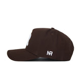 The Rutgers Americano Hat (B2B) is a brown snapback crafted from high-quality cotton, shown from the side with a structured fit, white NR embroidery near the back, and a partially visible white design on the front.