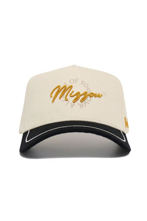 The Mizzou Tigers ALOYO Hat by No Rivals features “Mingou” embroidered in gold cursive, smaller surrounding text, a black brim with white outline, snapback adjustment, a gold side logo, and is made of high-quality beige cotton.