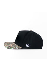 The No Rivals App State Camo Hat - Trailblazer Edition (B2B) features a black snapback design, a camouflage brim, white NR initials embroidered on the side, and is crafted from high-quality cotton. Side profile shown on white background.