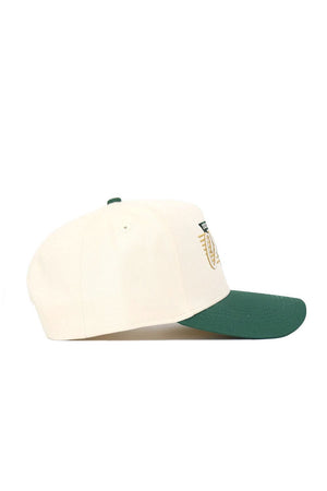 The No Rivals UNC Charlotte Triangle Game Cap Hat is a cream snapback with a green brim, seen from the side. It features a partially visible front logo in gold and green embroidery and offers a structured fit.