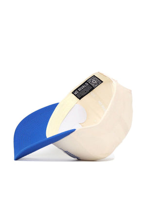 The No Rivals Tulsa Triangle Game Cap Hat is a cream-colored, structured baseball cap with a blue brim, shown angled from below to reveal the inside label reading "NO RIVALS," resting on a white surface.