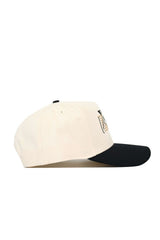 The No Rivals Vanderbilt Triangle Game Cap Hat is a beige baseball cap with a black curved brim, shown from the side. It features a structured fit and has a small embroidered front patch, partially visible in this view.
