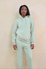 Person wearing a light green hoodie and pants against a beige background