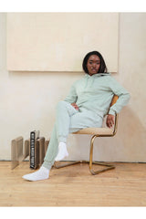 Person wearing a light green tracksuit sitting on a chair in a minimalistic room.