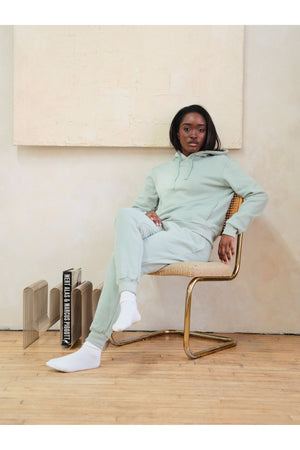 Person wearing a light green tracksuit sitting on a chair in a minimalistic room.