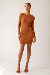 A woman modeling a fitted, long-sleeve mini dress in a warm camel brown color, paired with matching brown strappy high-heeled sandals, against a plain light gray studio background.