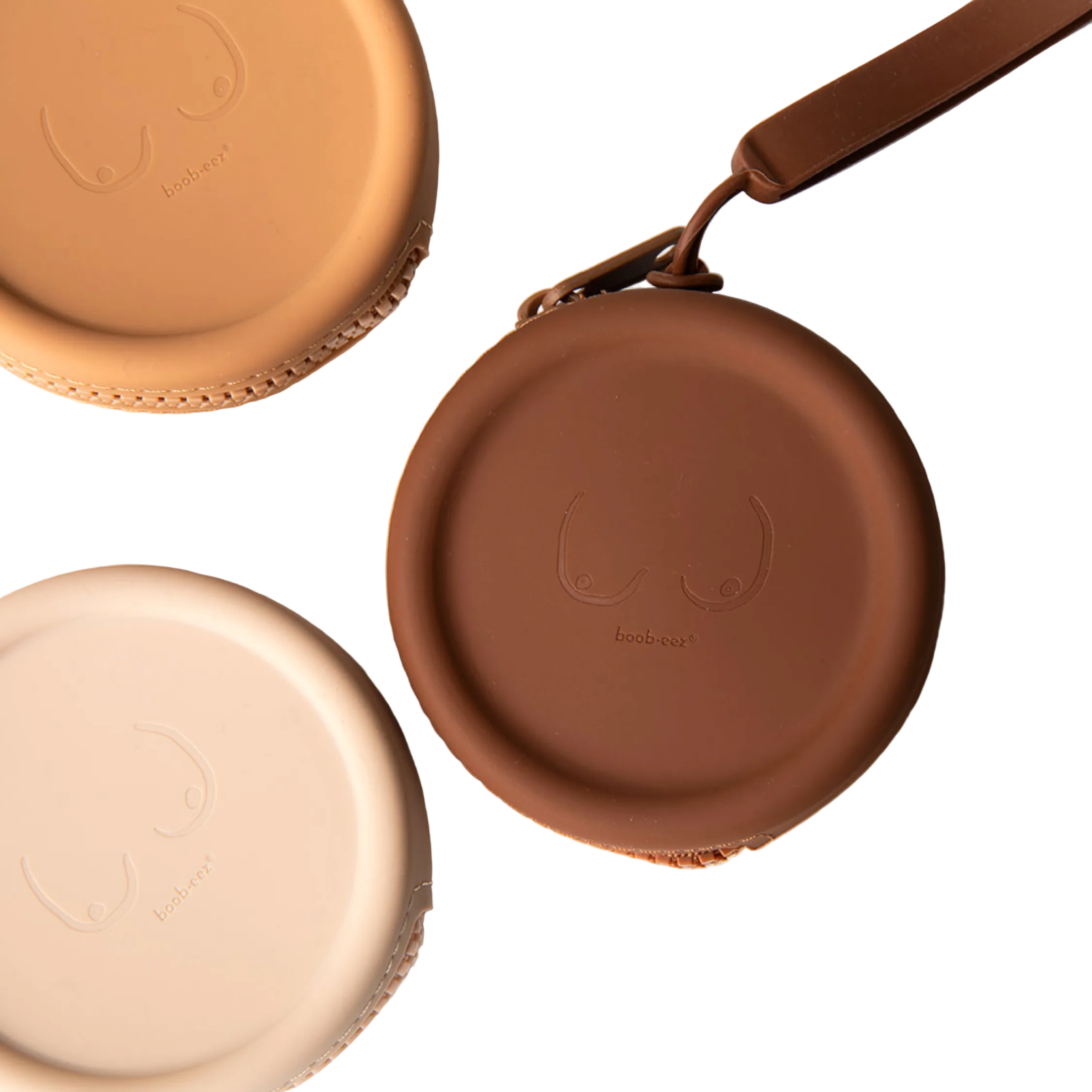 Product shot of our reusable Silicone Travel Cases for Headlight Hiders in Light Nude, Medium Nude and Dark Nude, with Headlight Hiders laying underneath the Silicone Travel Cases, against a white background