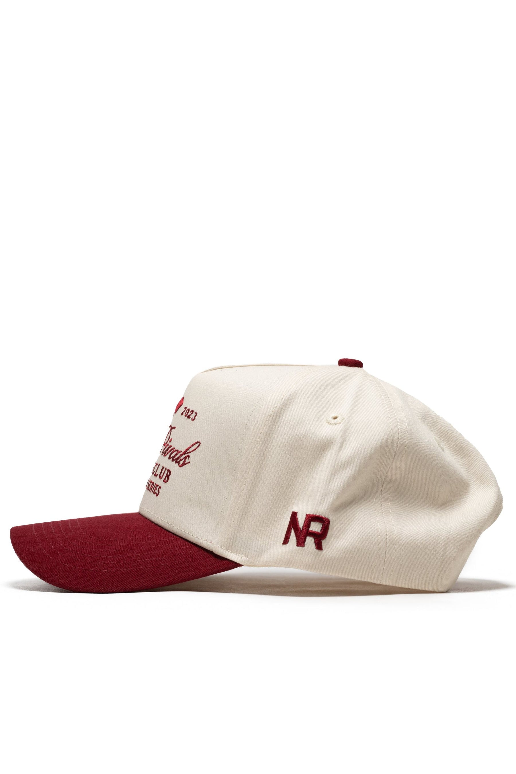 The No Rivals Sports Club Pickleball Hat - Classic Red is a structured cream snapback with a maroon brim, button, and embroidered NR text on the front and side. Made from high-quality cotton, it’s shown in profile against a white background.