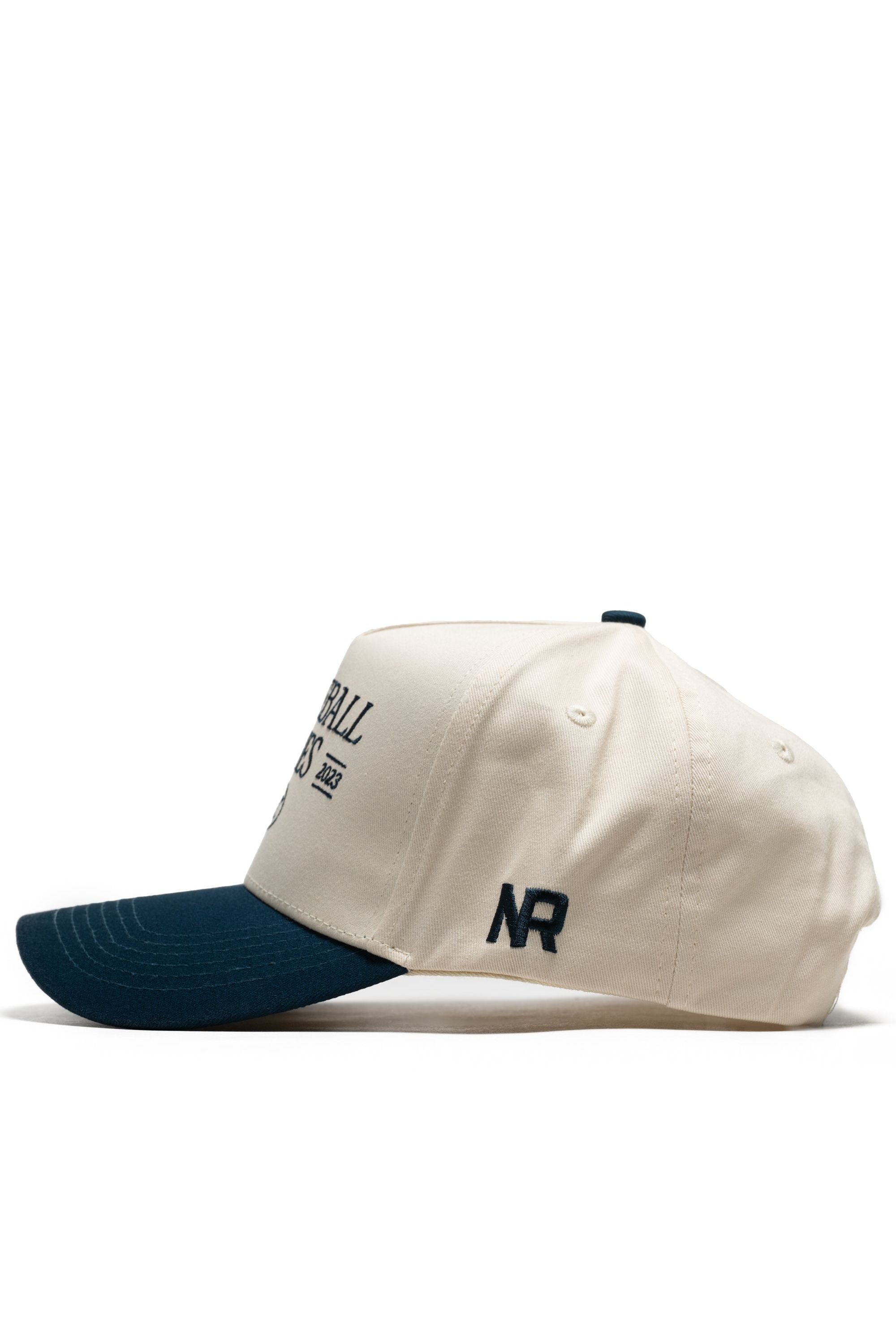 Side view of the No Rivals Old School Pickleball Hat - Classic Blue, a cream-colored snapback with a dark blue brim. Features black NR embroidery on the side and black text on the structured cotton front.