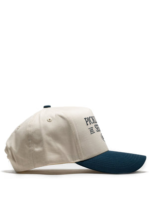 The No Rivals Old School Pickleball Hat - Classic Blue is shown in a side view. This cream cotton snapback features a dark blue brim and black "PICKLEBALL EST. SERVE" text on the front against a plain white background.
