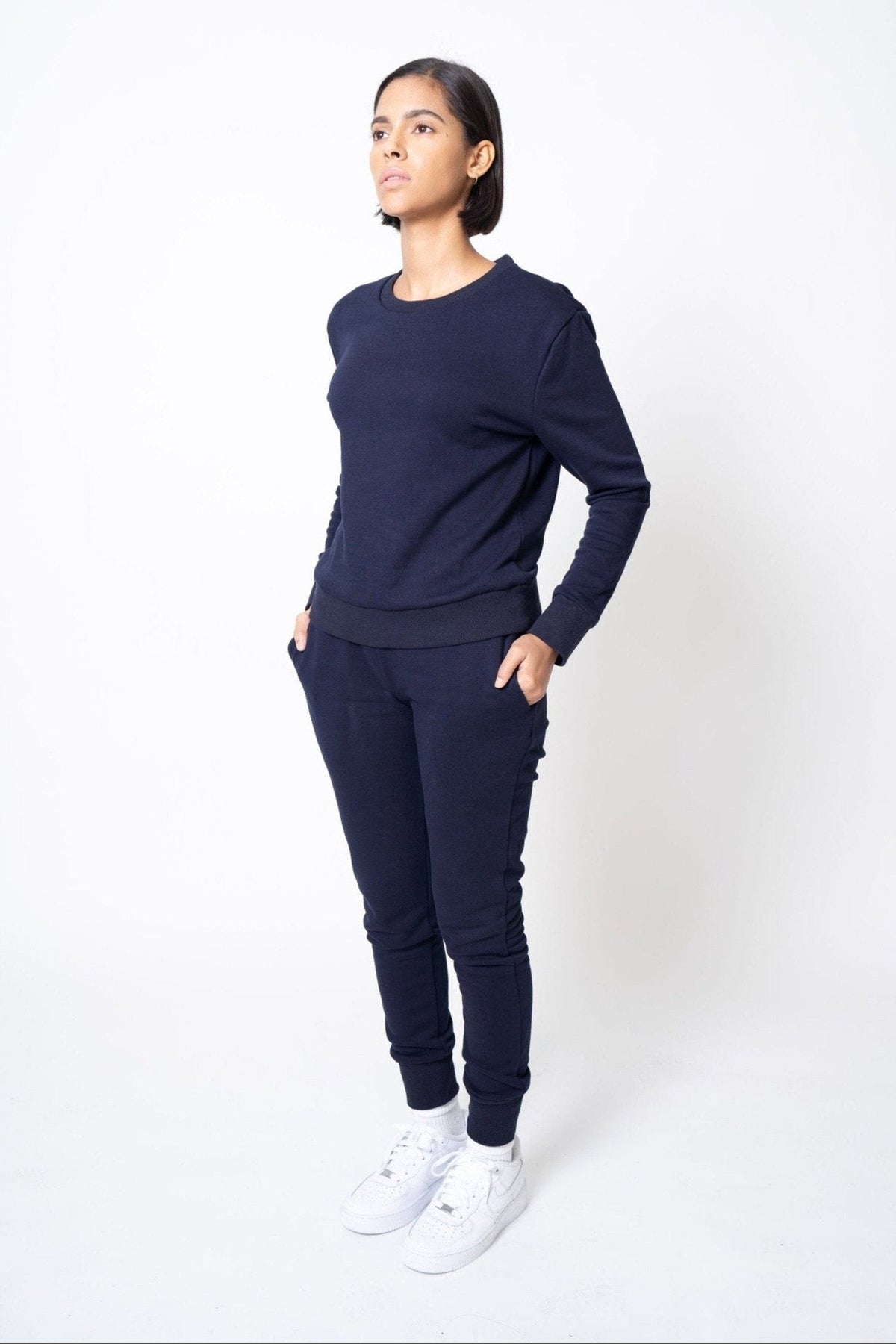 Person wearing a navy blue outfit with white sneakers on a white background