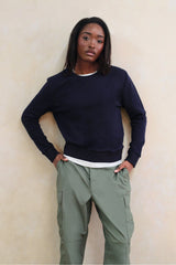 Person wearing a navy sweater and green cargo pants against a beige wall