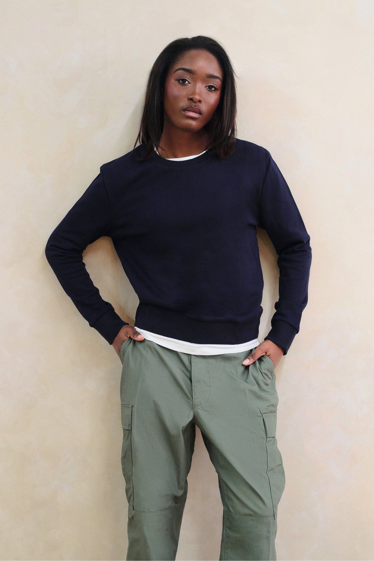 Person wearing a navy sweater and green cargo pants against a beige wall