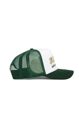 The No Rivals St.Pattys Trucker Hat features a green mesh back and bill, a white front panel with gold embroidered lettering and black text below, shown in left side profile view.