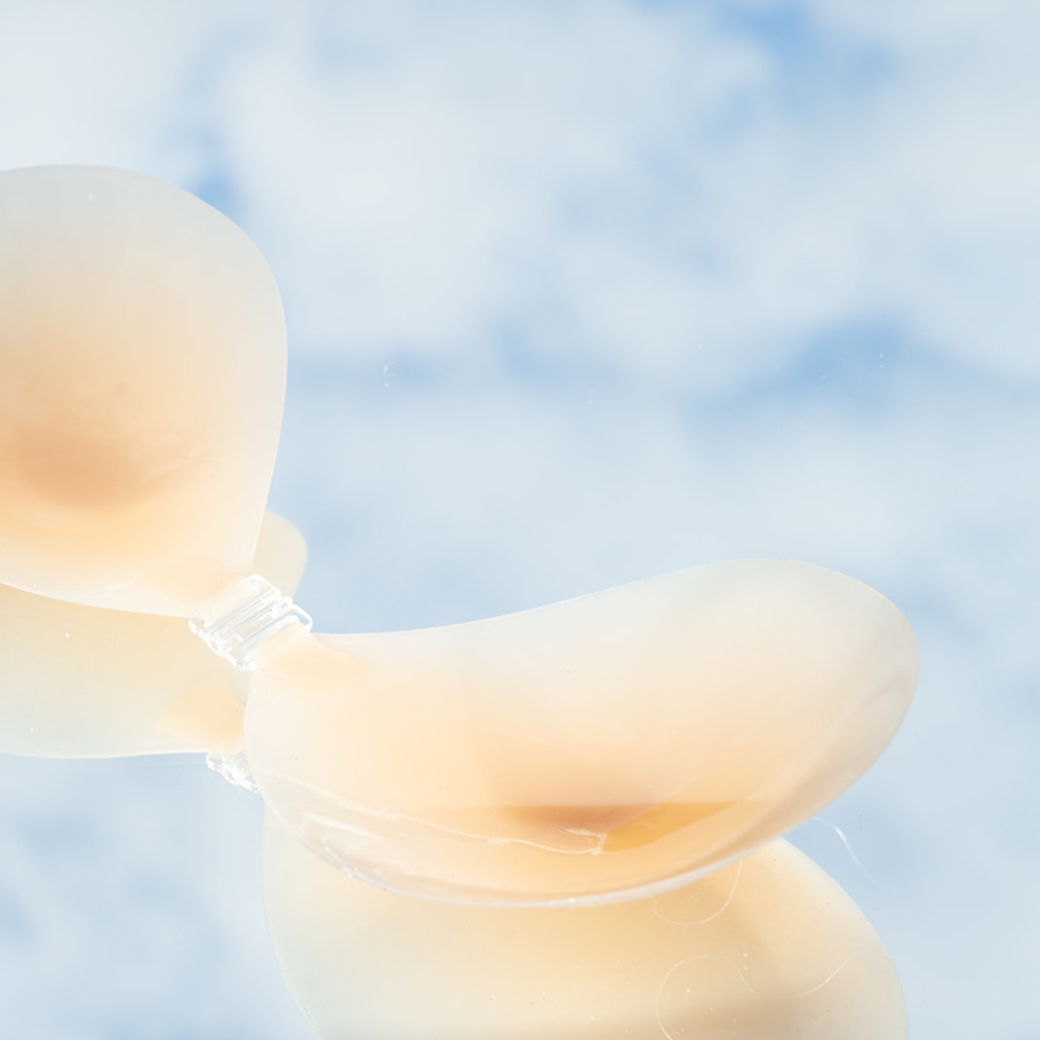 Product shot of reusable and sticky Silicone Stick-on Bra laying flat against mirrored sky background, close-up side shot of the Silicone Stick-on Bra showing the razor thin edges 